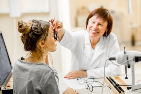 Senior woman ophthalmologist with young female patient during the consultation in the ophthalmological officeの写真素材