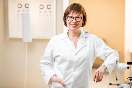 Portrait of a senior woman doctor in uniform standing in the ophthalmologic officeの写真素材