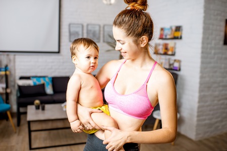 Portrait of a sports mother with her cute baby son hugging together at homeの写真素材