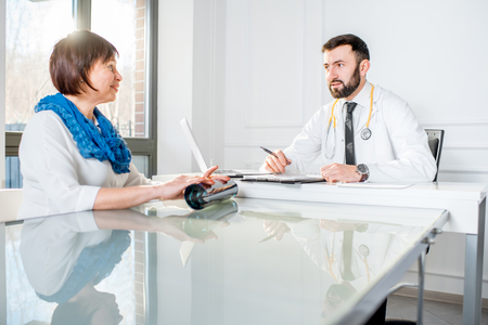 Older woman having a medical consultation with male doctor sitting at the white officeの写真素材