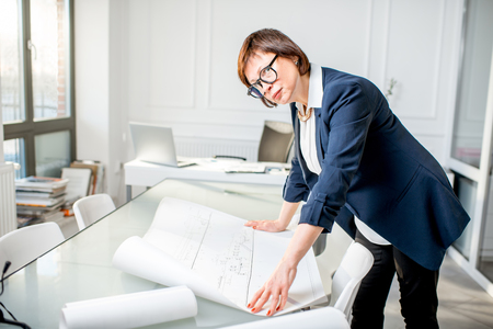 Elegant senior woman architect working with drawings standing in the white officeの写真素材