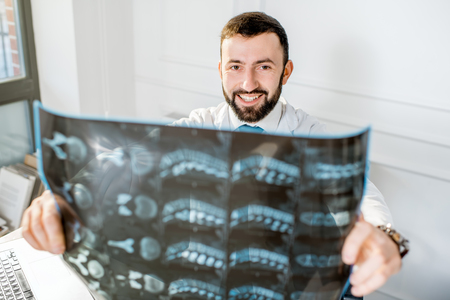 Handsome doctor looking on the x-ray print of human spine in the officeの写真素材