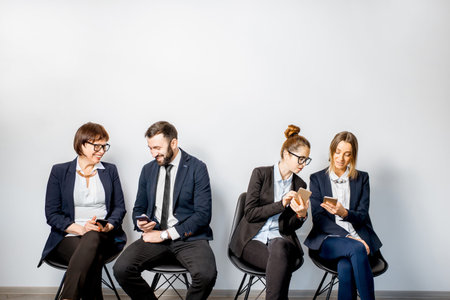 Business people using smart phones sitting in a row on the white wall background