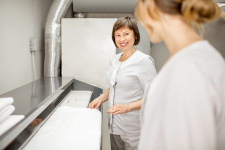 Laundress in unifrom working with professional ironing machine in the laundry