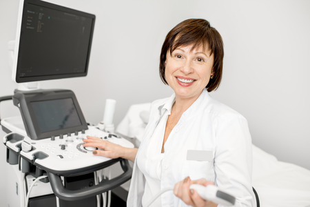 Portrait of a senior woman doctor in uniform with ultrasound equipment in the officeの写真素材