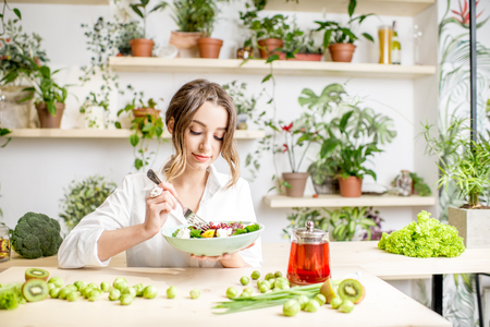 Young woman eating healthy food sitting in the beautiful interior with green flowers on the backgroundの写真素材