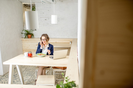 Businesswoman during the lunch sitting in the white cafe interior. Wide view with copy spaceの写真素材