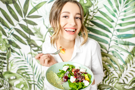 Portrait of a young woman with healthy food on the beautiful wall with green plants drawings on the backgroundの写真素材
