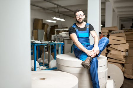 Portrait of a worker in uniform sitting on the big paper rolls at the packaging manufacturingの写真素材