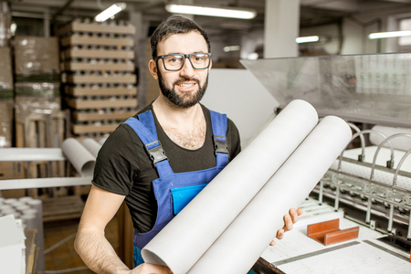 Portrait of a handsome worker in unifrom standing with paper tubes at the old printing manufacturingの写真素材