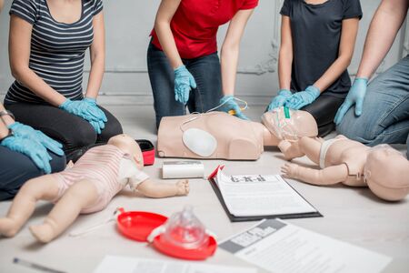 Young woman instructor clinging contacts on a dummy teaching how to make defibrillation during the first aid group training indoorsの写真素材
