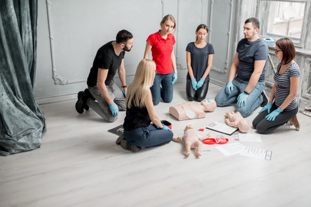 Group of people learning how to make first aid heart compressions with dummies during the training...