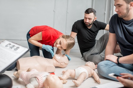 Young woman instructor showing how to throw back dummies head for breathing during the first aid group training indoorsの写真素材