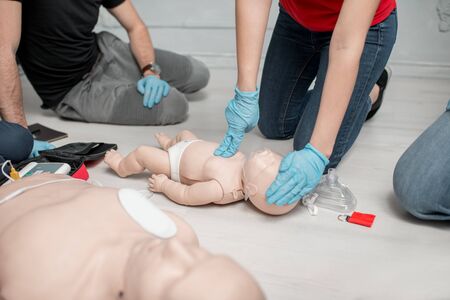 Instructor showing how to make chest compressions on a baby dummy during the first aid training indoorsの写真素材