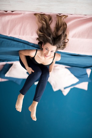 Portrait of a young woman in bra and leggings lying on the bed relaxing in the blue cozy bedroom at homeの写真素材