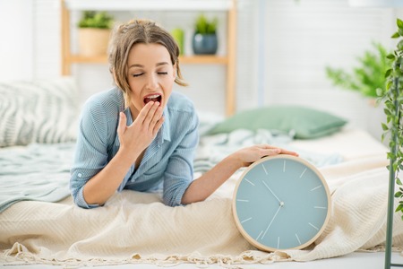 Portrait of a beautiful sleepy woman turning off the alarm clock lying in the cozy and bright bedroom at homeの写真素材