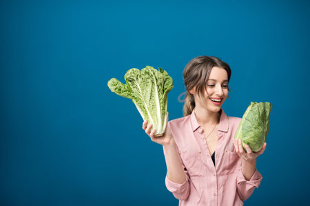 Portrait of a young woman with green lettuce on the blue wall backgroundの写真素材