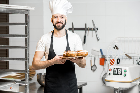 Portrait of a handsome confectioner stnading with sweet pastry in the professional kitchenの写真素材