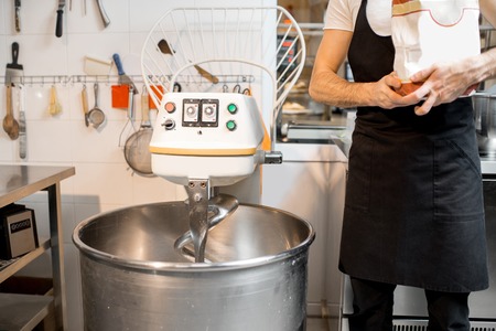 Baker standing with flour bag near the professional kneader machine at the bakery. Cropped image with no faceの写真素材