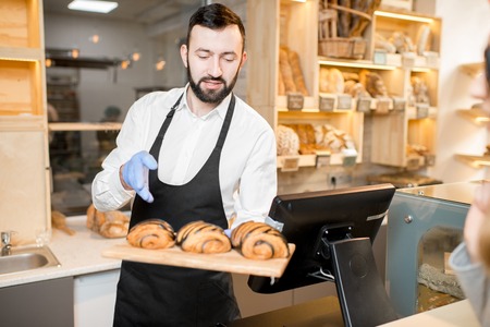 Bread seller offering delicious croissants standing in the store with bakery productsの写真素材