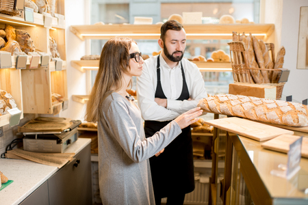 Young female owner of the bakery store with bread seller talking together in the shopの写真素材