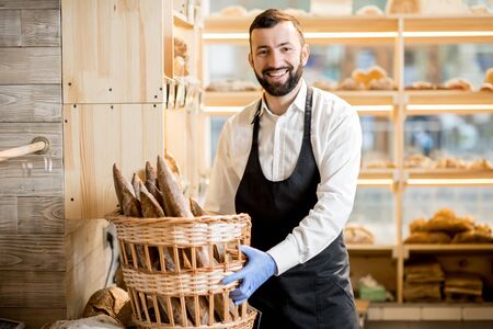 Bread seller with basket full of baguettes in the store with bakery productsの写真素材