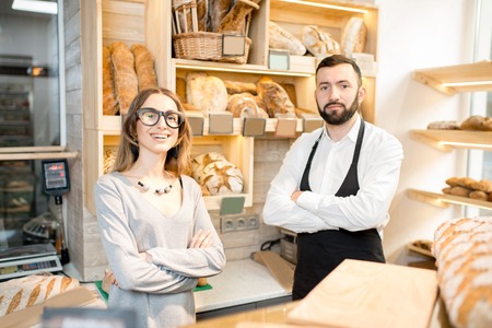 Young female owner of the bakery store with bread seller talking together in the shopの写真素材