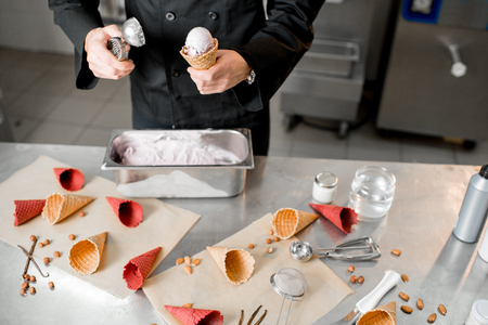 Chef filling waffle cone with ice cream on the table with ingredients and tools for ice cream makingの写真素材