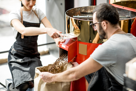 Couple pouring roasted coffee beans into the paper bag from the roaster machine for sellingの写真素材