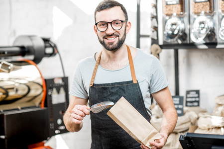 Male seller in uniform filling bag with coffee beans working in the coffee storeの写真素材