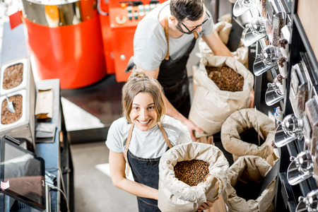 Portrait of a two happy sales persons in uniform standing with bags full of coffee beans in the coffee storeの写真素材