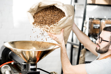 Man pouring coffee beans into the roaster machine indoorsの写真素材