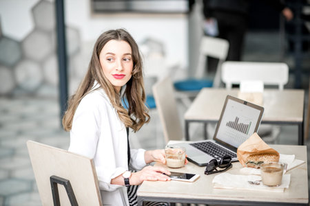Portrait of an elegant business woman sitting with laptop during the coffee break in the modern cafe interiorの写真素材