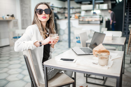 Portrait of an elegant business woman sitting with laptop during the coffee break in the modern cafe interiorの写真素材