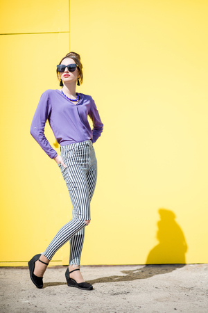 Portrait of a stylish woman dressed in pink shirt on the yellow wall background outdoorsの写真素材