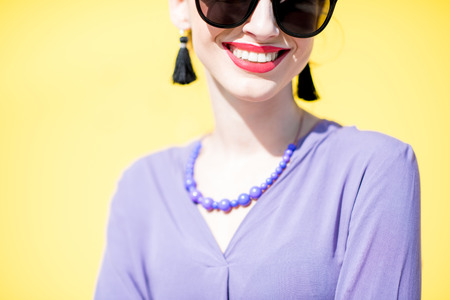 Close-up portrait of a stylish woman dressed in pink shirt with sunglasses on the yellow wall background outdoorsの写真素材