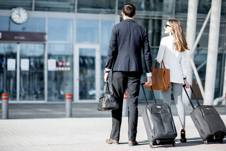 Business couple walking together to the airport entrance carrying suitcases and bagsの写真素材