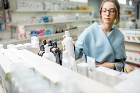 Woman taking a bottle with cosmetics from the shelf of the pharmacy supermarketの写真素材