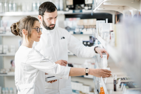 Woman and man pharmacists supervising medicaments in the pharmacy storeの写真素材