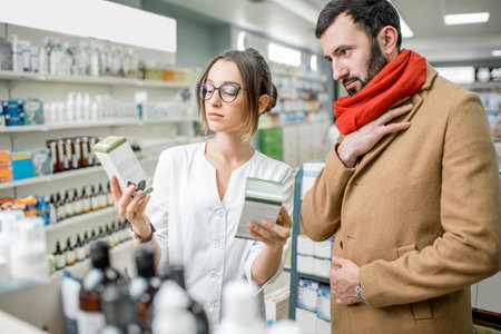 Young woman pharmacist choosing medicine with male client dressed in coat and scarf in the pharmacy...