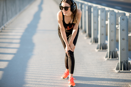 Sports woman holding knee having a trauma during the morning run on the bridgeの写真素材