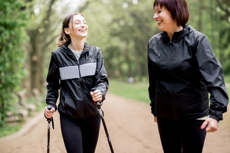 Young and elder woman in black sportswear walking with hiking sticks in the parkの写真素材