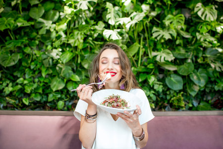 Young and beautiful woman enjoying heathy salad sitting at the vegetarian restaurant with living...