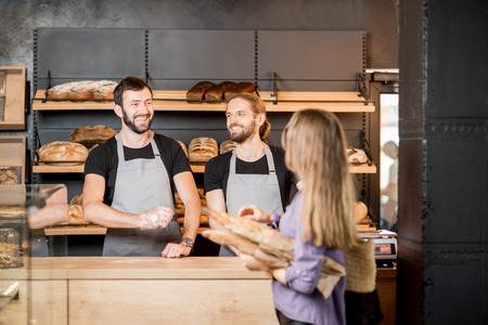 Young woman client buying bread at the bakery shop with handsome male sellersの写真素材