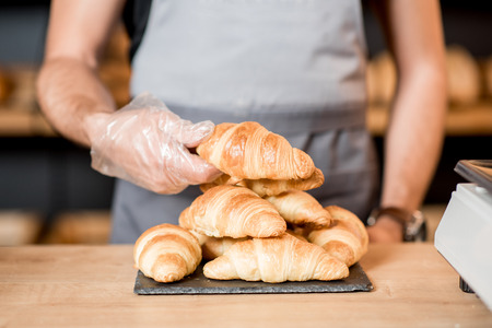 Seller serving croissant on the plate at the counter of the bakery shop, Close-up viewの写真素材