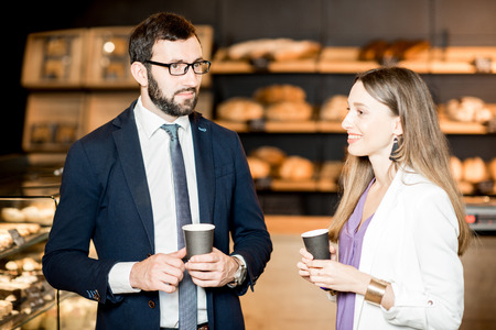 Business people talking during the coffee break standing near the counter of the pastry shopの写真素材