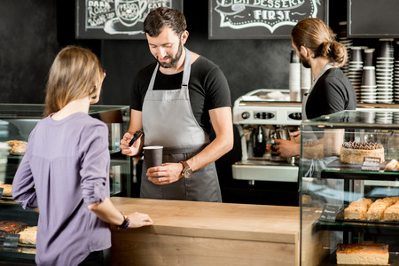 Handsome barista making coffee for a young woman customer standing at the counter of the coffee shopの写真素材