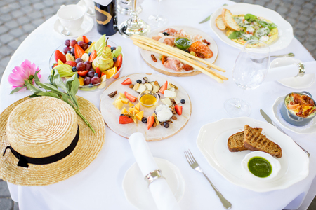 Top view on the well-serviced table with romantic breakfast, flowers and hat outdoorsの写真素材