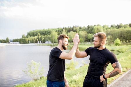 Male friends giving five after the sports training outdoors near the lake