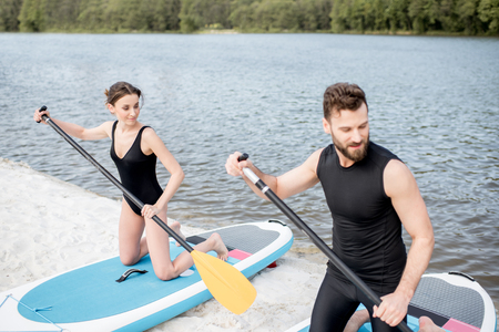 Couple in black swimwear learning to row on the stand up paddleboard on the beachの写真素材